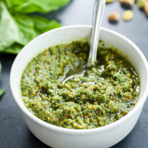 Pistachio basil pesto recipe in white pottery bowl with pistachios on the side