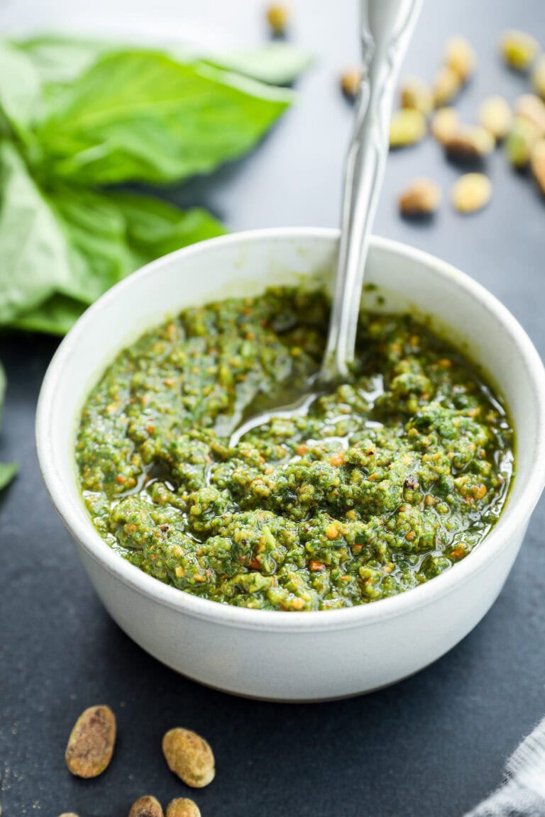 Pistachio basil pesto recipe in white pottery bowl with pistachios on the side