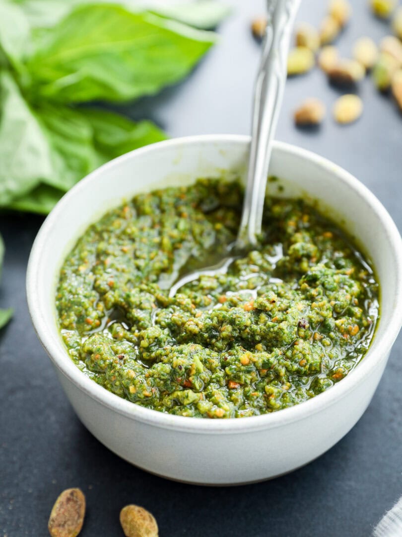 Pistachio basil pesto recipe in white pottery bowl with pistachios on the side