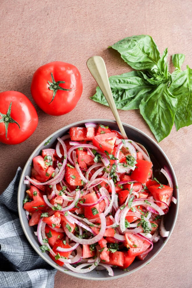 Tomato onion salad in large bowl with fresh tomatoes and fresh basil leaves