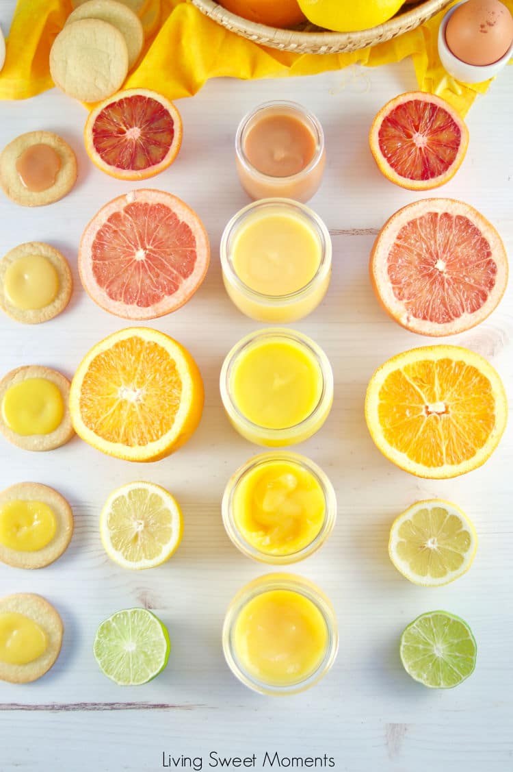 Top-down view of citrus curds in jars, surrounded by halved grapefruits, oranges, lemons, limes, and cookies topped with curd, arranged neatly on a white surface with a yellow cloth.