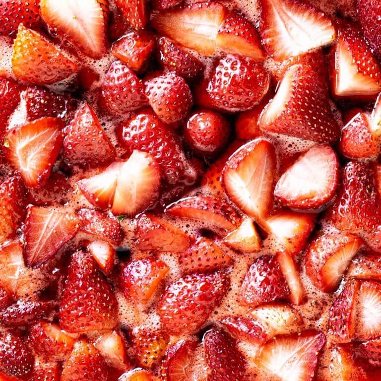 Close-up of fresh strawberries, cut into pieces and coated with a glossy, juicy glaze, showing vibrant red colors and bubbly liquid between the fruit pieces.