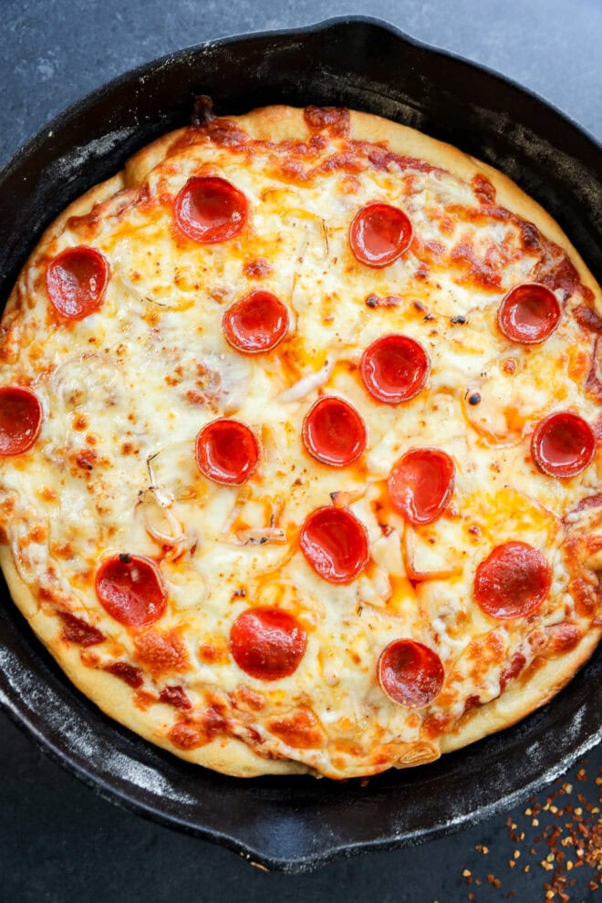 A freshly baked spicy pizza in a black cast iron skillet, topped with melted cheese and evenly spaced pepperoni slices.