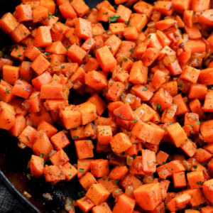 Diced sweet potatoes sautéed with herbs and spices in a black skillet, showing a vibrant orange color and slightly crispy texture.