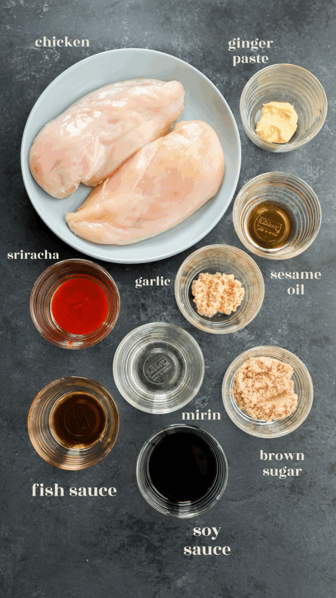 Two raw chicken breasts on a plate, surrounded by bowls of ginger paste, sesame oil, brown sugar, soy sauce, mirin, fish sauce, garlic, and sriracha—everything you need for a flavorful Asian Chicken Marinade. Each ingredient is clearly labeled.