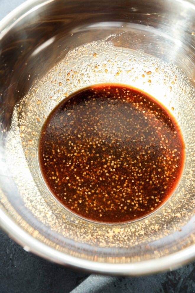 A metal mixing bowl containing a dark, slightly thick Asian Chicken Marinade with visible flecks of seasoning and spices.