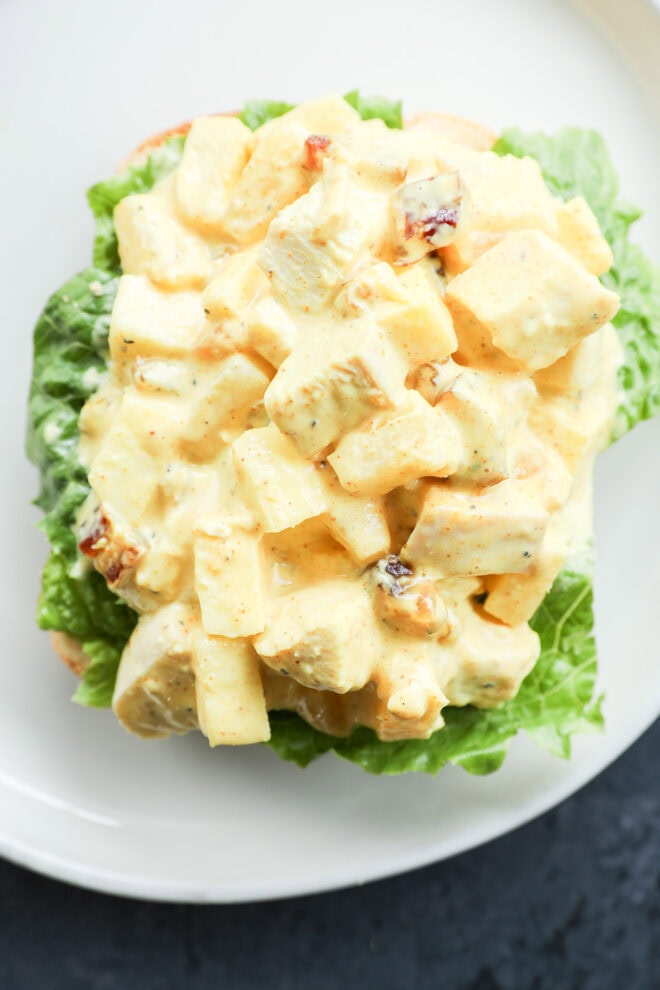 An open-faced sandwich with creamy salad on a bed of green leaf lettuce, served on a white plate.