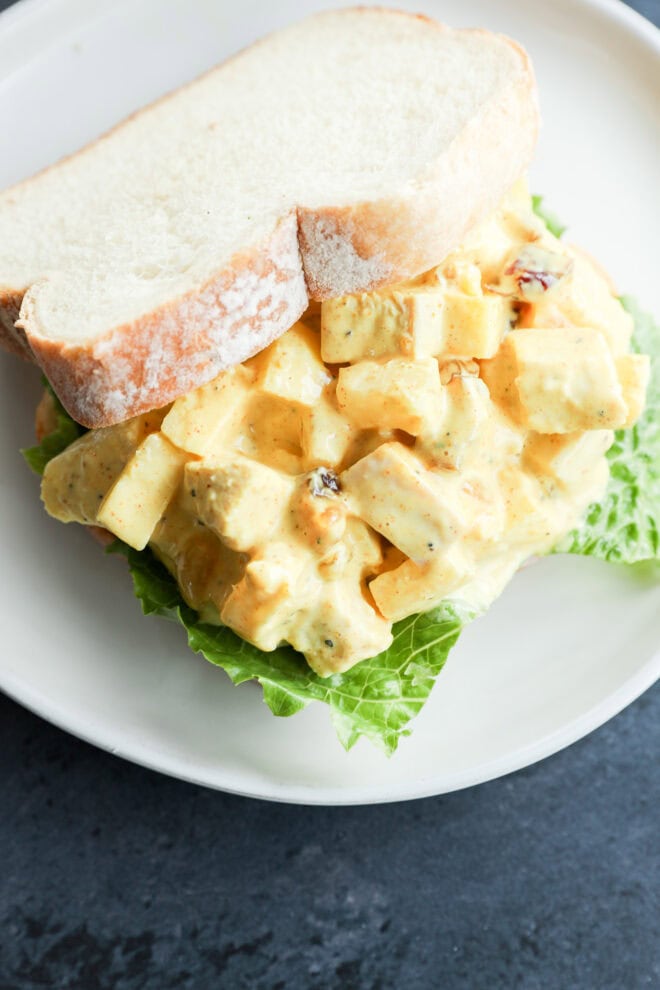 A sandwich on white bread filled with curried chicken salad—diced chicken, lettuce, and yellow curry dressing—served on a white plate.