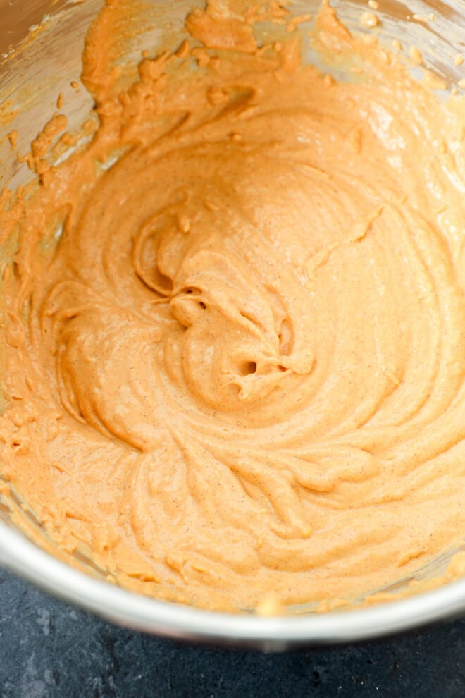 A metal mixing bowl filled with creamy, light brown batter, swirled smoothly, sitting on a dark countertop.