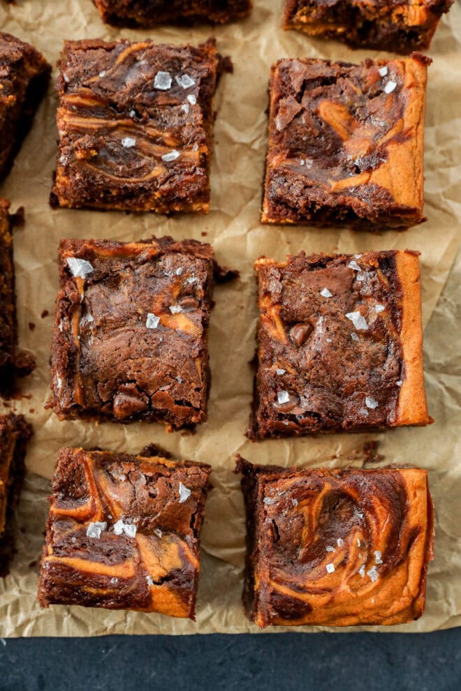 Nine chocolate brownies with a marbled pattern and sprinkled sea salt on top, arranged neatly on parchment paper.