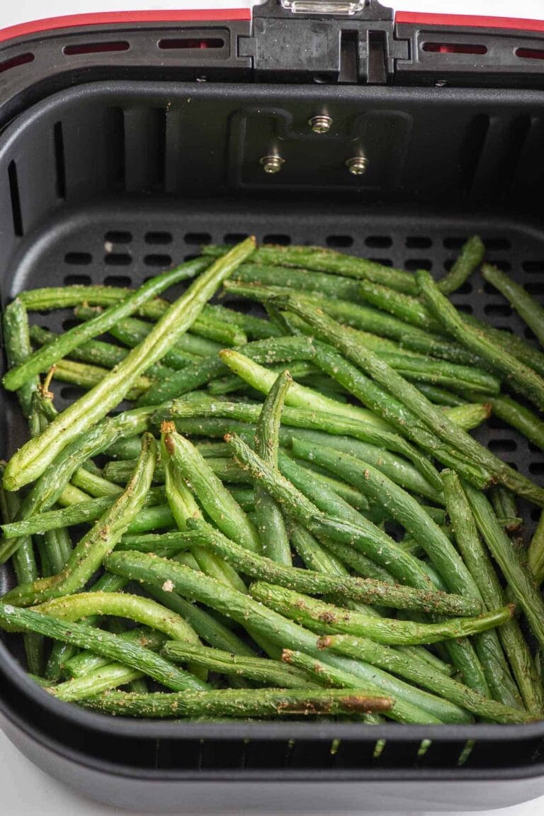 Fresh green beans coated with seasoning are arranged in a single layer inside the basket of an air fryer, ready to be cooked.
