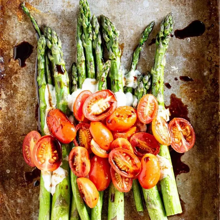 Roasted asparagus spears topped with halved cherry tomatoes and drizzled with melted cheese and balsamic glaze on a baking sheet.