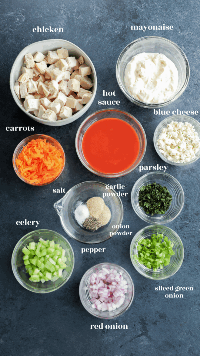 A top-down view of bowls containing diced chicken, mayonnaise, hot sauce, blue cheese, shredded carrots, chopped parsley, seasonings, and veggies—perfect inspiration for meal prep for buffalo chicken salad.