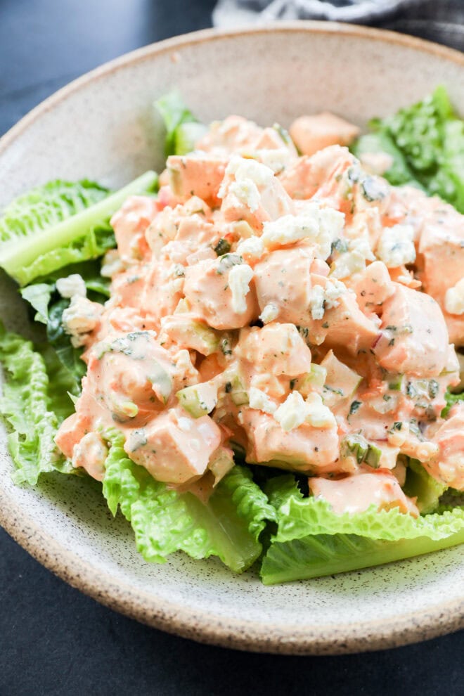 A bowl of salad with chunks of chicken mixed in a creamy orange dressing, placed on a bed of fresh green romaine lettuce leaves for buffalo chicken salad.