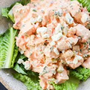 A bowl of chopped chicken salad mixed with a creamy dressing and crumbled blue cheese, served on a bed of fresh romaine lettuce leaves. It's buffalo chicken salad.