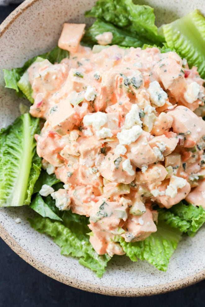 A bowl of chopped chicken salad mixed with a creamy dressing and crumbled blue cheese, served on a bed of fresh romaine lettuce leaves. It's buffalo chicken salad.