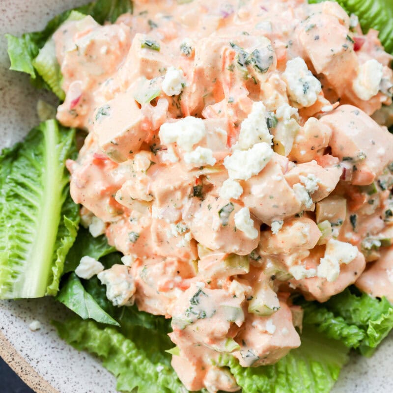 A bowl of chopped chicken salad mixed with a creamy dressing and crumbled blue cheese, served on a bed of fresh romaine lettuce leaves. It's buffalo chicken salad.