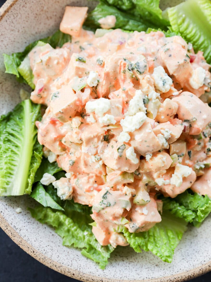 A bowl of chopped chicken salad mixed with a creamy dressing and crumbled blue cheese, served on a bed of fresh romaine lettuce leaves. It's buffalo chicken salad.
