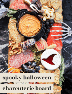 A Halloween charcuterie board featuring meats, cheeses, crackers, fruits, nuts, and dips is decorated with plastic skeleton hands and served on a marble table. Text reads: spooky halloween charcuterie board.