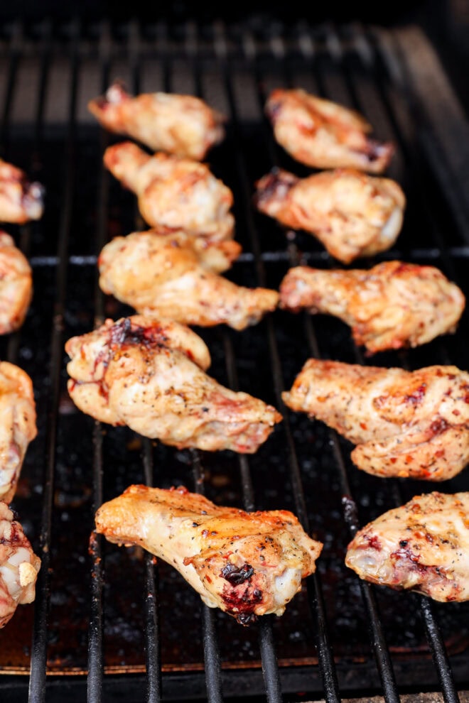 Grilled chicken wings cooking on a barbecue grill, seasoned and slightly charred, with grill marks visible on the meat and grill grates.