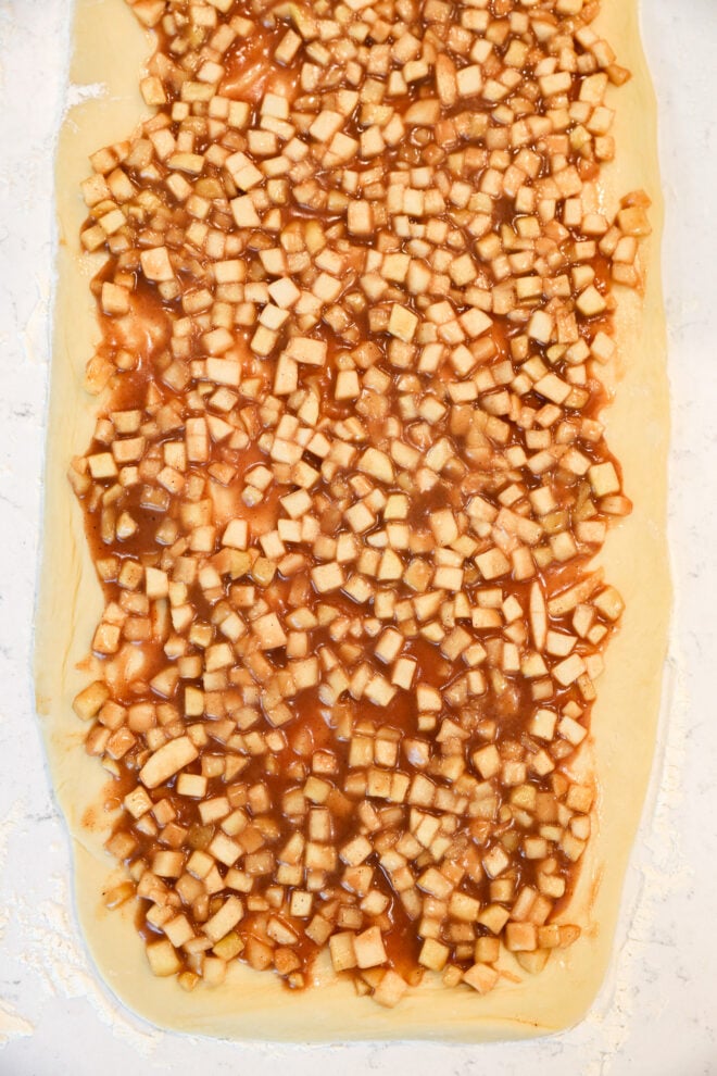 Dough rolled out flat and topped with a mixture of small diced apples and cinnamon filling, just like Apple Pie Filled Cinnamon Rolls, ready to be rolled or baked.