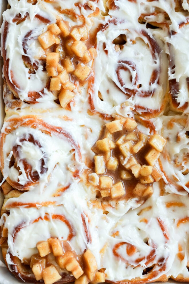 Close-up of Apple Pie Filled Cinnamon Rolls topped with creamy white frosting and diced cooked apples in cinnamon sauce, creating a gooey and appealing texture.