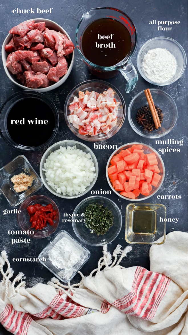 Top-down view of Instant Pot Beef Bourguignon ingredients, including chuck beef, beef broth, red wine, bacon, mulling spices, onion, carrots, garlic, thyme and rosemary, tomato paste, cornstarch, olive oil, honey&mdash;and all-purpose flour.