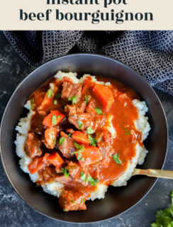 Overhead view of a black bowl filled with mashed potatoes topped with Instant Pot Beef Bourguignon and carrots, garnished with herbs. A gold spoon rests in the bowl. Text reads instant pot beef bourguignon and www.cakenknife.com.