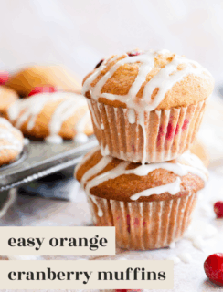 Two orange cranberry muffins stacked on top of each other, drizzled with white icing. More orange cranberry muffins and fresh cranberries appear in the background. Text reads “easy orange cranberry muffins.”.