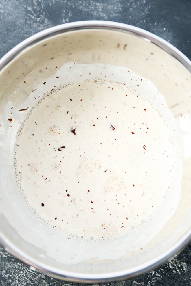 A metal mixing bowl filled with cream and small pieces of chopped chocolate, ready to be mixed together for ganache.