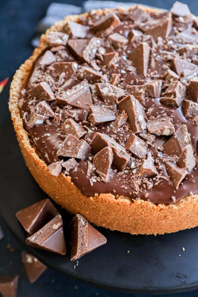 A chocolate pie with a crumbly crust, topped with a glossy chocolate layer and generous chunks of milk chocolate pieces.