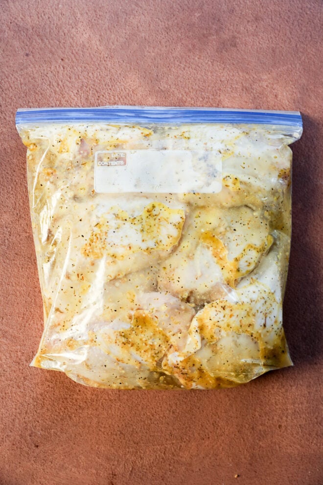 A clear ziplock bag filled with raw chicken pieces marinating