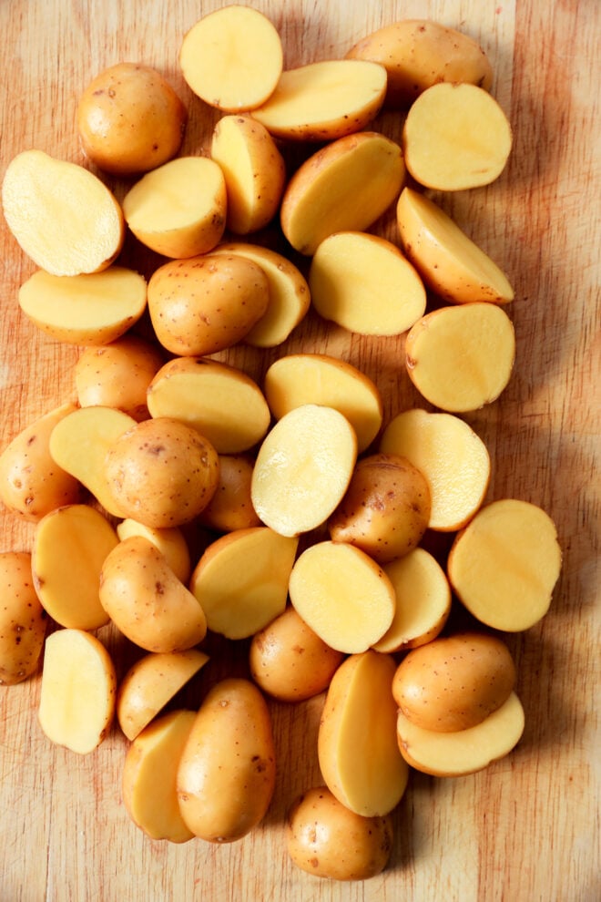 A pile of small yellow potatoes, some whole and some cut in half, arranged on a wooden cutting board