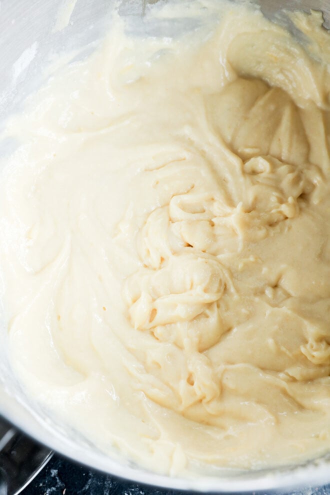 Close-up of a bowl containing smooth, creamy lemon ricotta cake batter, with visible swirls and folds in the mixture.