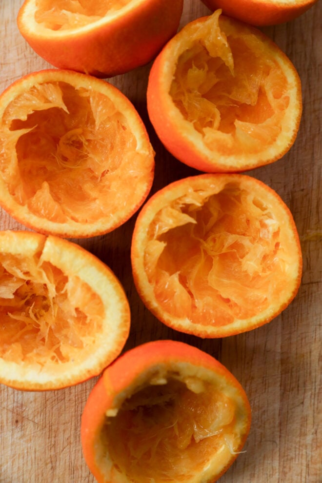 Several orange halves are shown with their insides scooped out, exposing the fibrous inner surfaces arranged on a wooden surface.