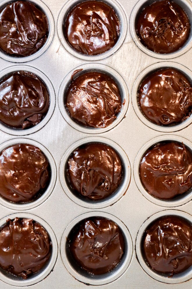 A muffin tin filled with twelve compartments, each containing glossy, uncooked Brownie Bites batter ready to be baked.