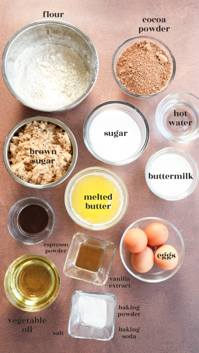 A top-down view of brownie cake baking ingredients in bowls and cups, including flour, cocoa powder, hot water, buttermilk, brown sugar, sugar, melted butter, eggs, vegetable oil, espresso powder, vanilla extract, salt, and baking soda.