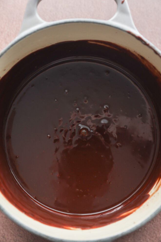 A white saucepan filled with glossy, melted chocolate ganache