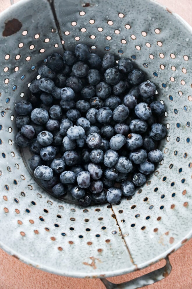 A metal colander filled with fresh blueberries, seen from above.