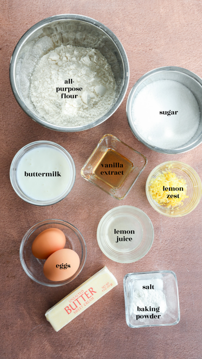 Top-down view of ingredients for a lemon loaf cake in bowls and containers, labeled: all-purpose flour, sugar, buttermilk, vanilla extract, lemon zest, eggs, lemon juice, butter, salt, and baking powder on a brown surface.