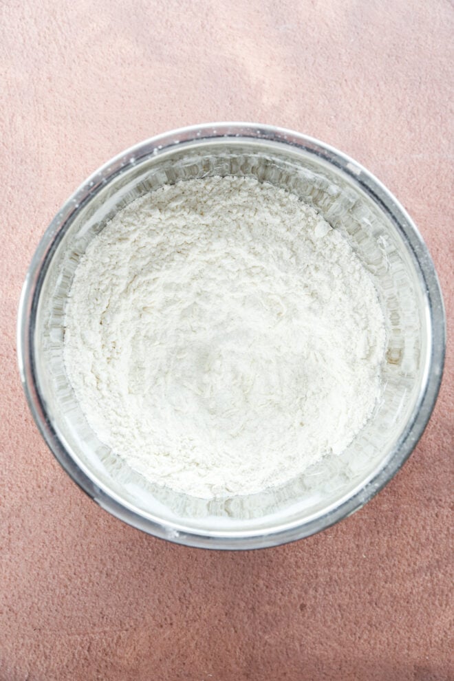 A metal mixing bowl filled with white flour, ready to be used for baking.