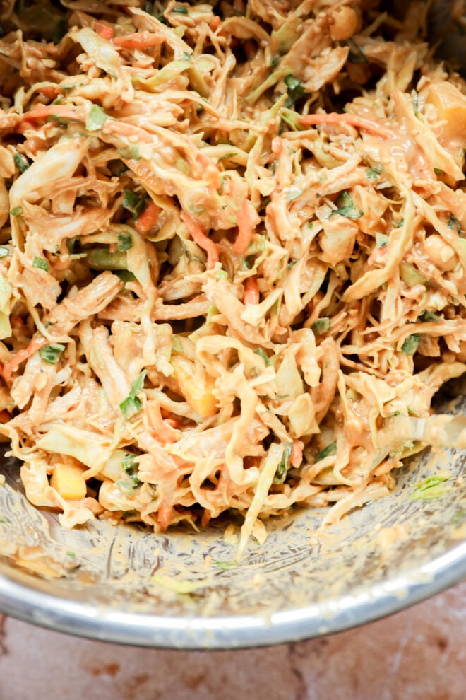 Close-up of a bowl of creamy coleslaw with shredded cabbage, carrots, and herbs mixed in a thick, orange-tinted dressing.