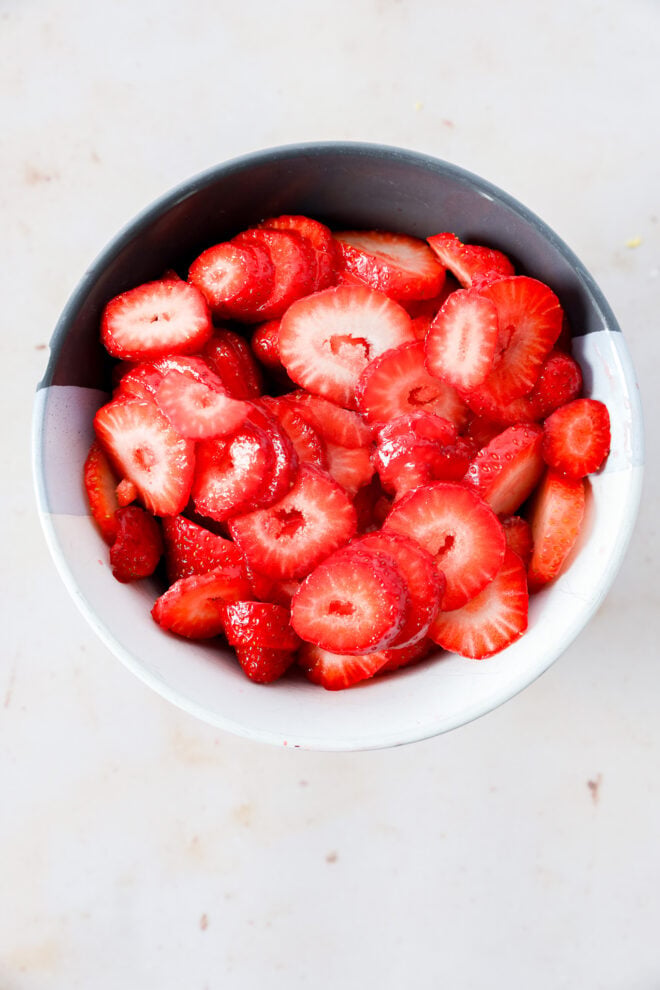 A bowl filled with freshly sliced strawberries on a light-colored surface.