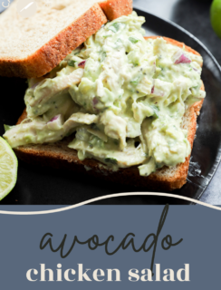 A sandwich with creamy avocado chicken salad on whole wheat bread sits on a black plate, garnished with a lime wedge and part of an avocado. Text on the image highlights this delicious avocado chicken salad.