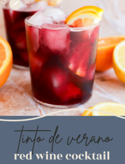 Two glasses of red wine cocktail with ice and orange slices sit on a light surface, surrounded by fresh orange wedges. The text on the image reads “Tinto de verano red wine cocktail.” Enjoy this refreshing twist on a classic red wine cocktail.