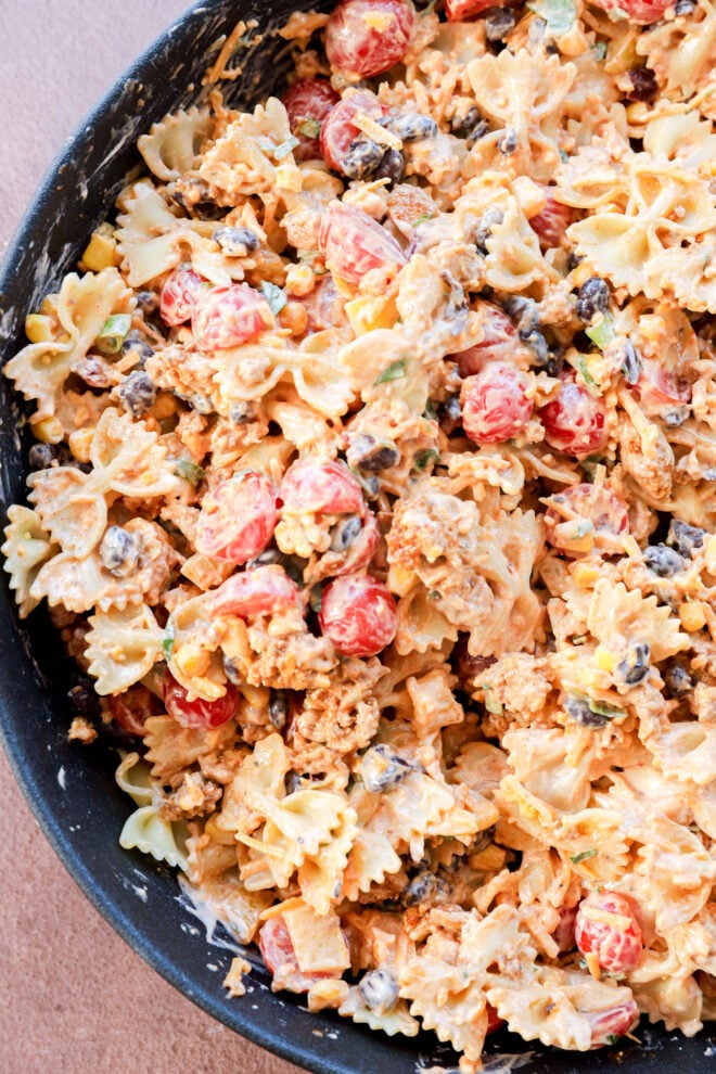 Close-up of Taco Pasta Salad featuring bowtie pasta, cherry tomatoes, black beans, ground meat, green onions, and a creamy orange dressing, all mixed together in a bowl.