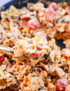A close-up of a spoonful of Taco Pasta Salad with creamy bowtie noodles, cherry tomatoes, black beans, green onions, and ground meat, with more of the flavorful dish blurred in the background.