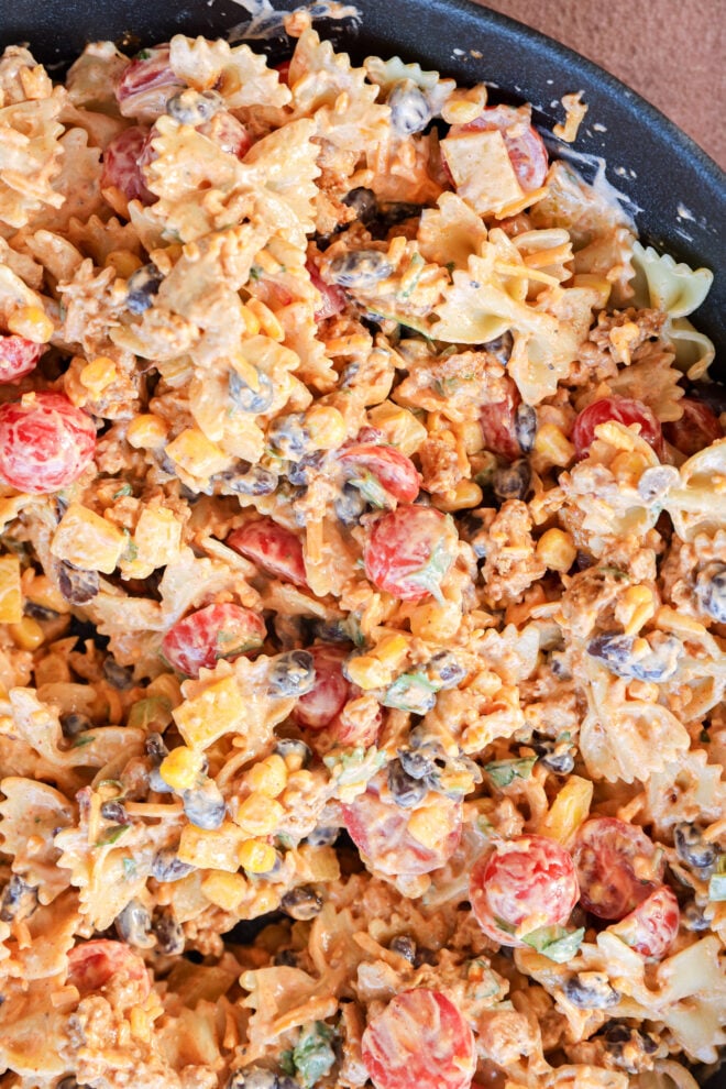 Close-up of a creamy Taco Pasta Salad with bowtie pasta, cherry tomatoes, corn, black beans, chopped green onions, shredded cheese, and a zesty creamy dressing all mixed together.