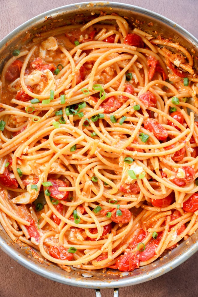 Creamy Burrata Pasta with Chili Crisp & Burst Tomatoes features spaghetti mixed with cherry tomatoes, green herbs, and a luscious creamy sauce in a skillet.