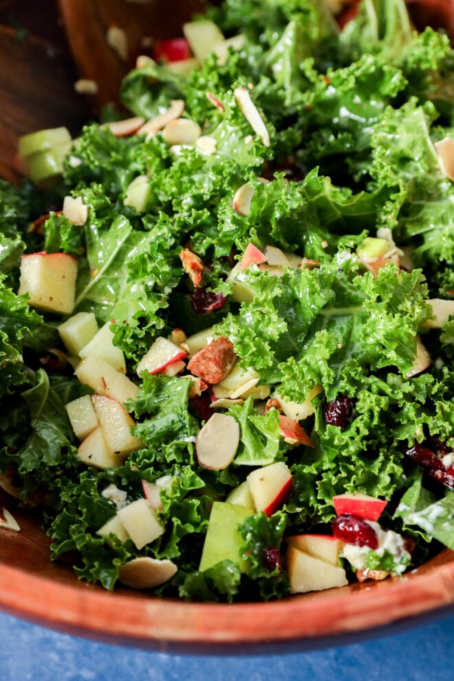 Apple and kale salad with chopped apples, dried cranberries, and sliced almonds in a wooden bowl.